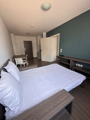 A hotel room with a bed, a desk, a chair, a wardrobe, and a television.