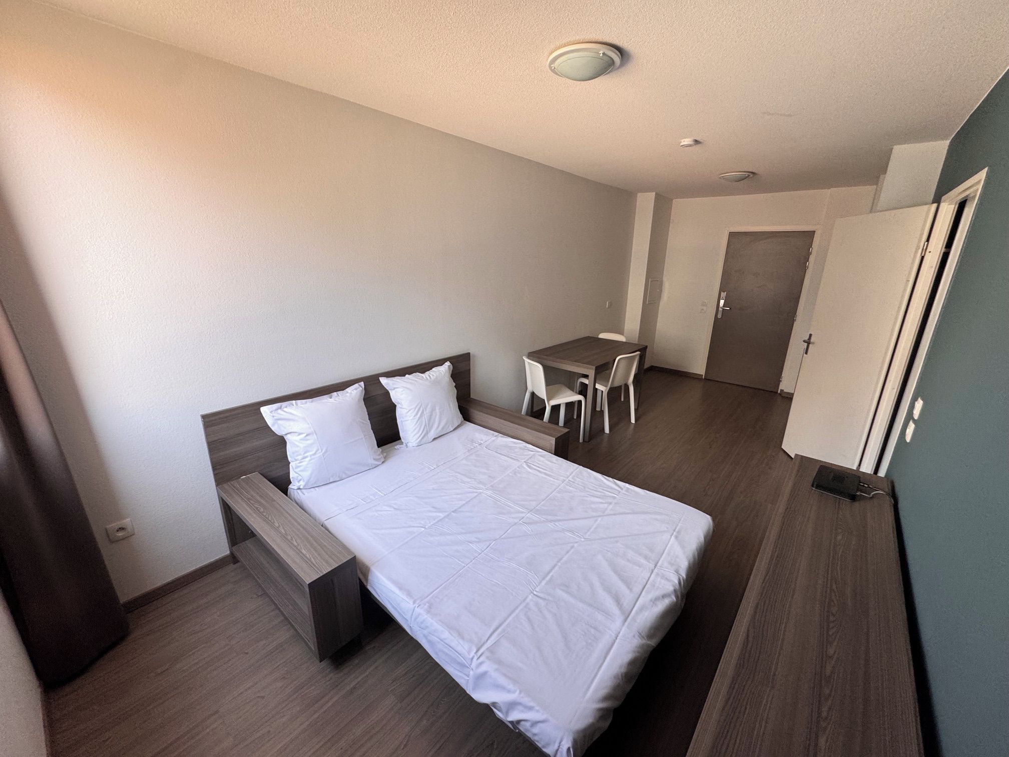 A hotel room with a bed, a desk, a chair, and a wardrobe.