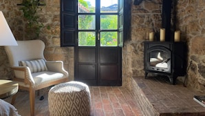A cozy room with a stone wall, a wooden chair, a round ottoman, a fireplace, and a window with shutters. - Luxurious villa Floravista for 12 people in Piloña (Valle, Piloña)