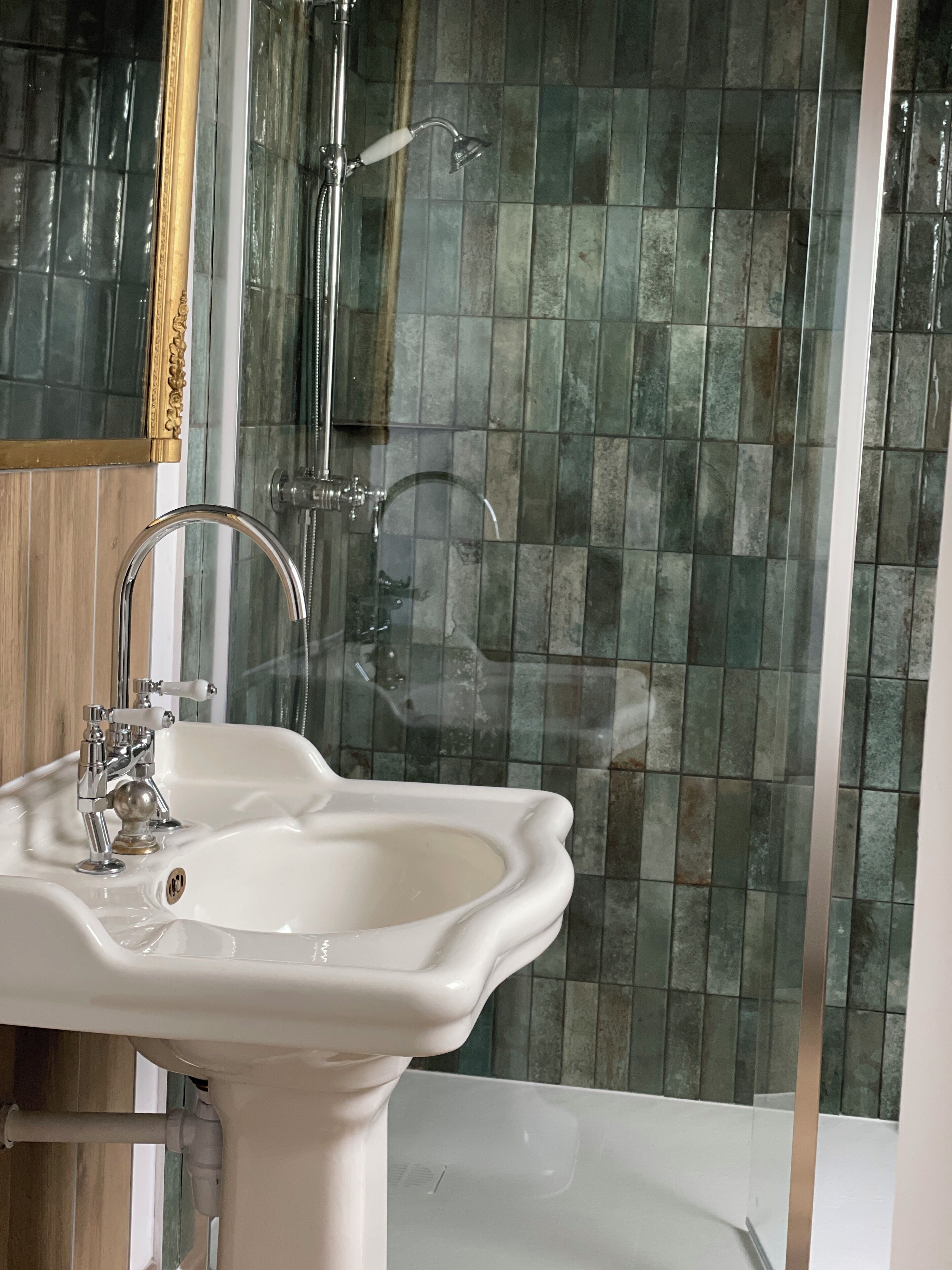Un baño con un lavamanos pedestal blanco, una ducha con puerta de cristal y pared de azulejos.