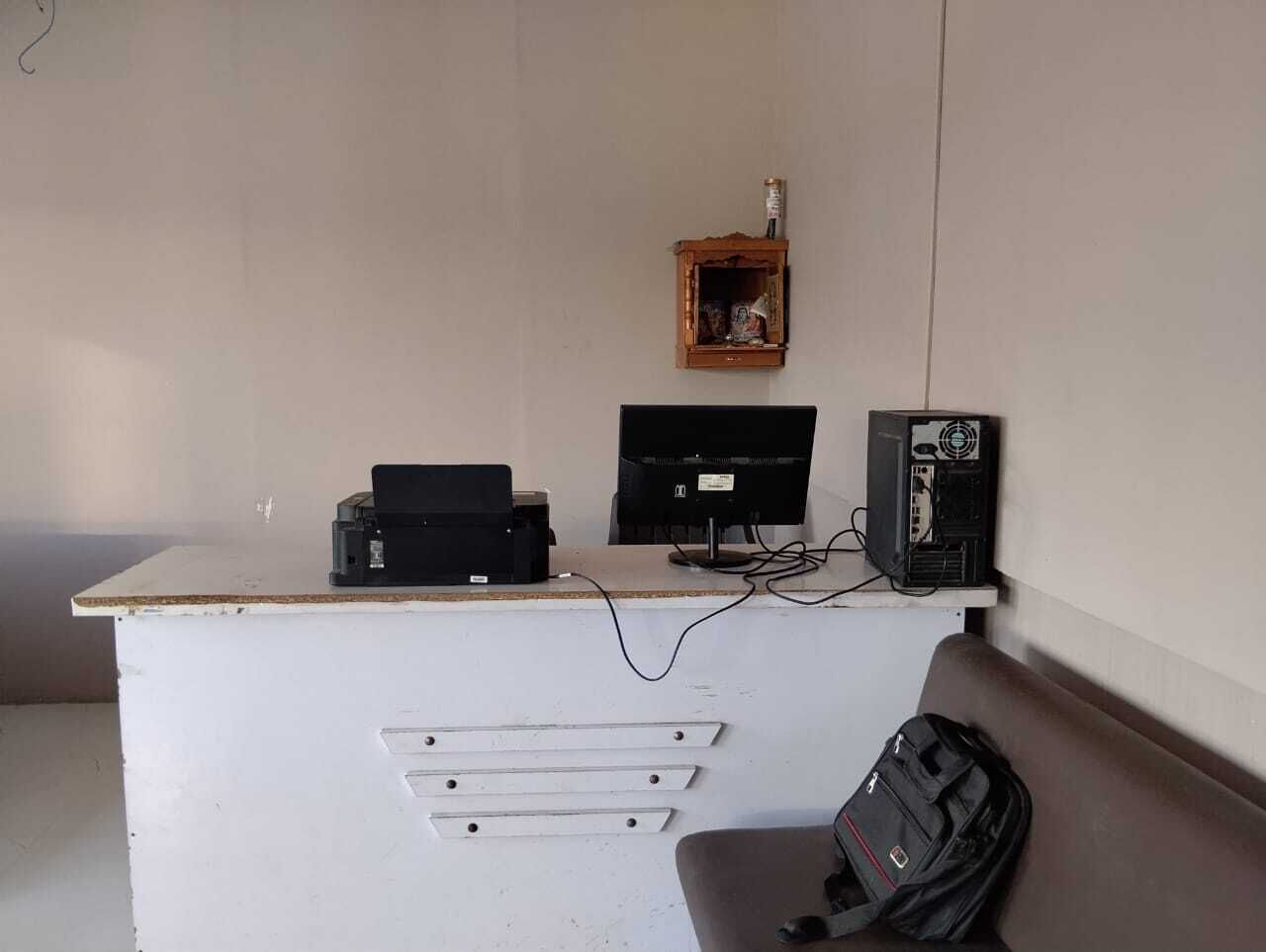 A white desk with a computer, printer, and a small wooden shelf with a bottle.