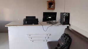 A white desk with a computer, printer, and a small wooden shelf with a bottle.