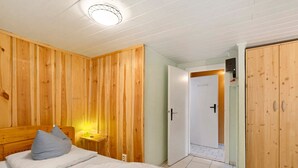 Un dormitorio con cabecera de madera, cama con ropa de cama blanca, mesita de noche con lámpara y un armario.