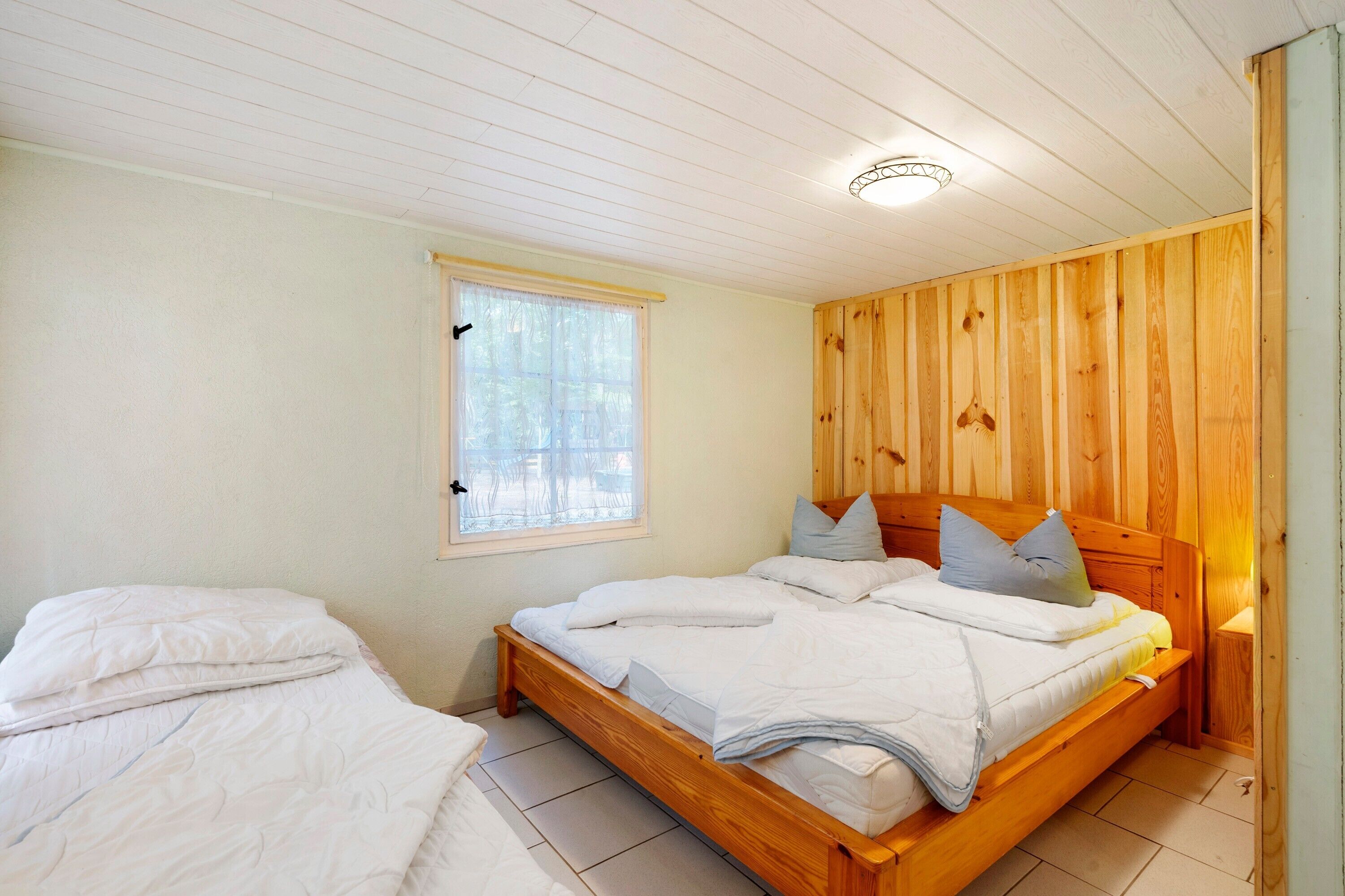 A bedroom with a wooden bed, a window with curtains, and a wooden wall panel.