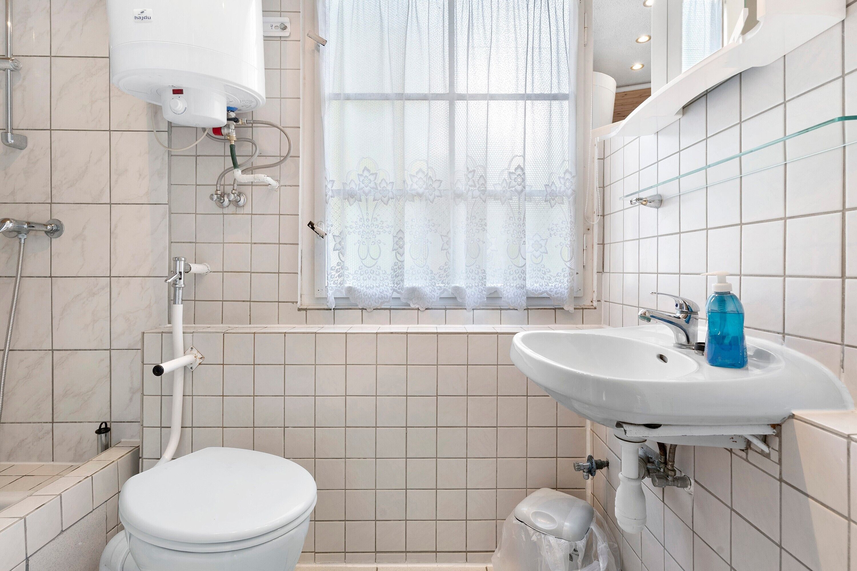 Un baño con inodoro, lavamanos, ducha y ventana con cortina.