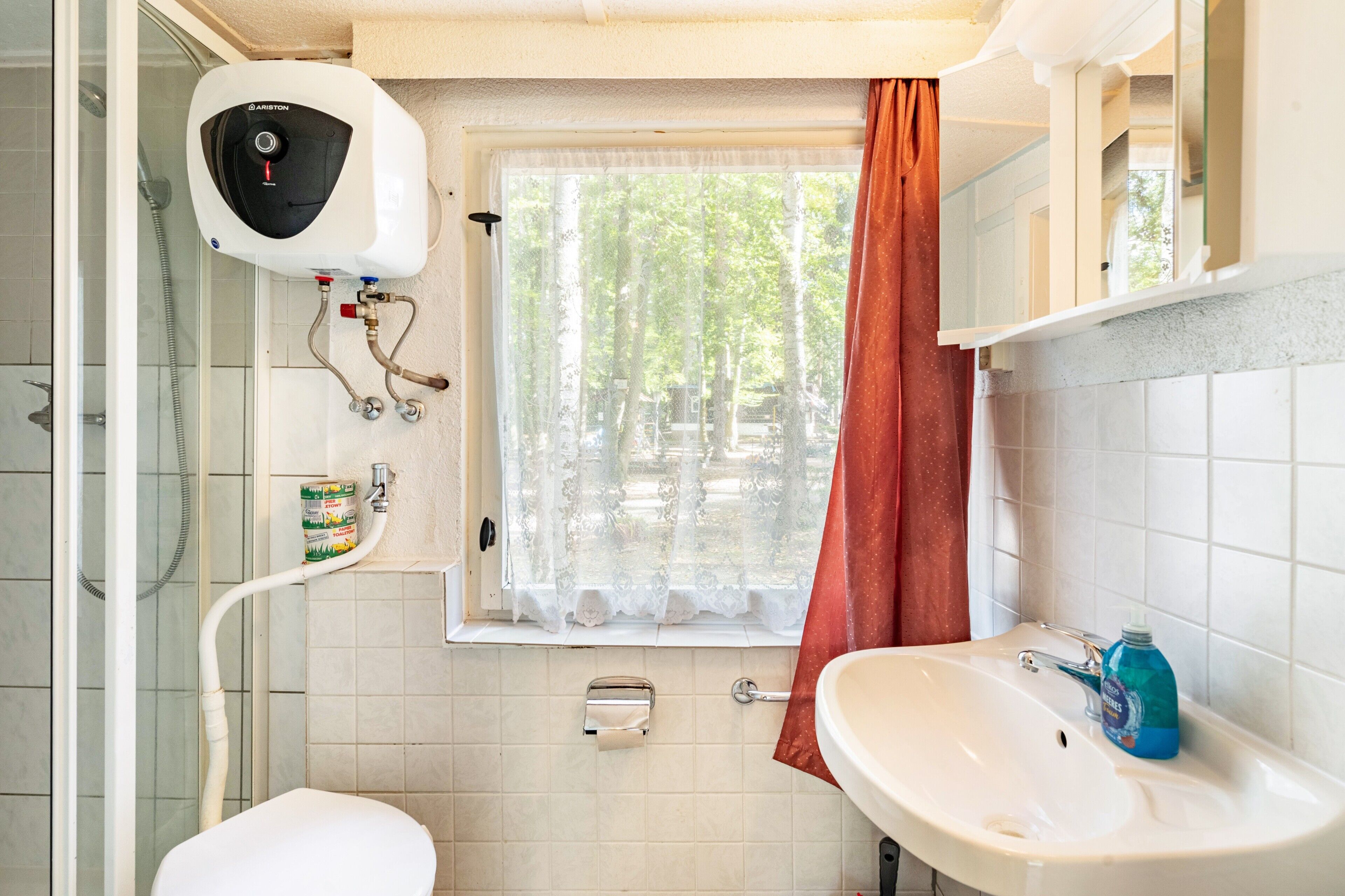 Un baño con inodoro, lavamanos, ducha y ventana con cortina.
