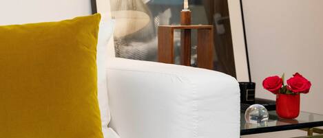 A white sofa with a mustard-colored pillow, a glass table with a red vase of roses, and a framed picture on the wall.
