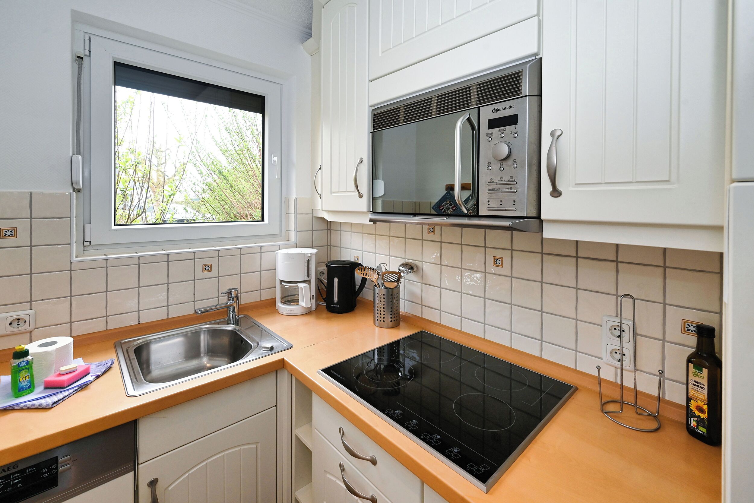 A kitchen with white cabinets, a stainless steel sink, a built-in microwave, and a black induction cooktop.