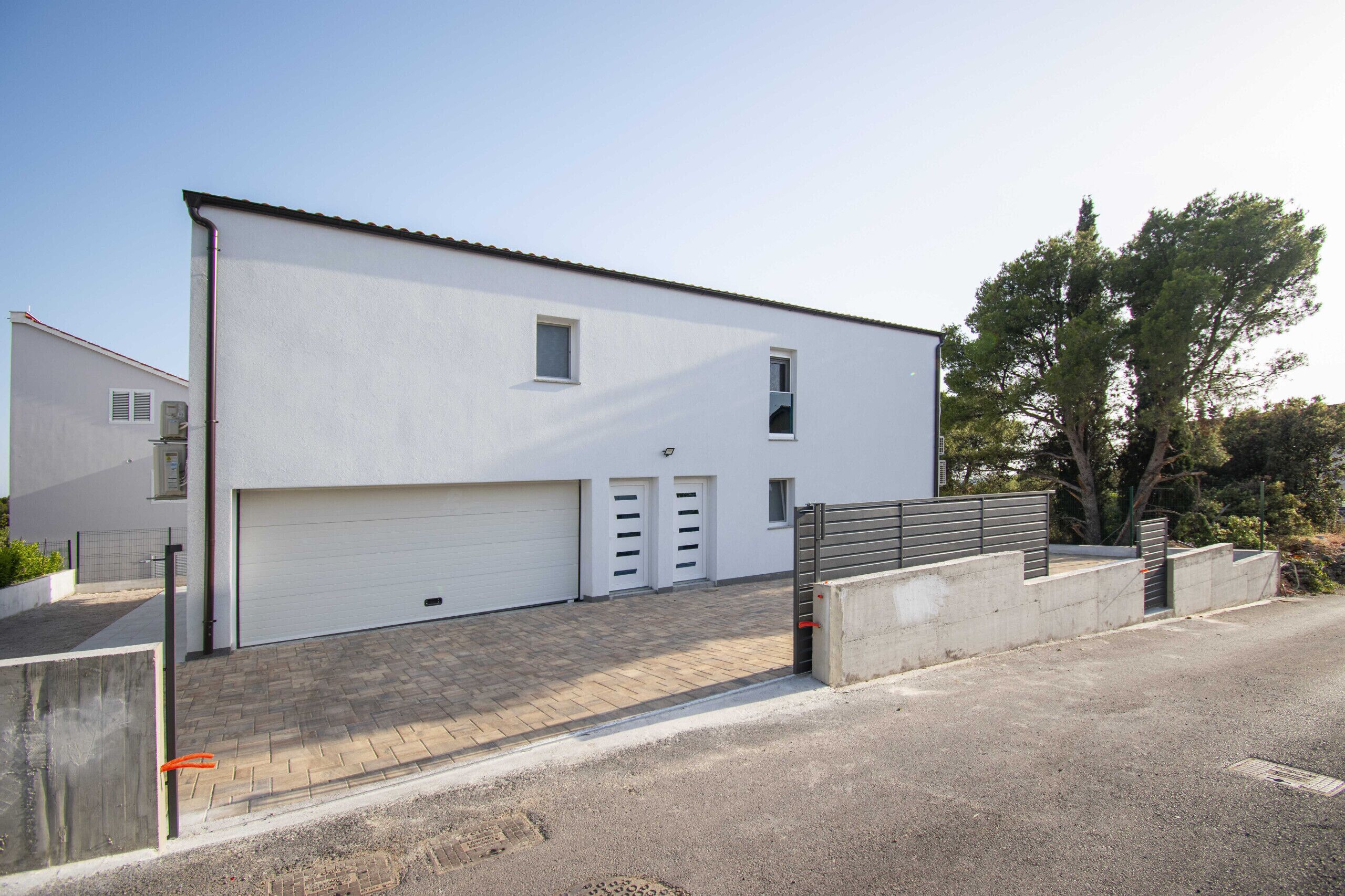 Ein modernes, zweistöckiges Gebäude mit weißer Fassade, einer Garage und einem gepflasterten Auffahrt.