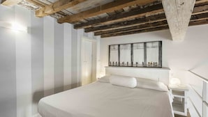 Ein Schlafzimmer mit einem großen Bett, Holzbalken an der Decke, einer weißen Wand und einem großen Fenster.
