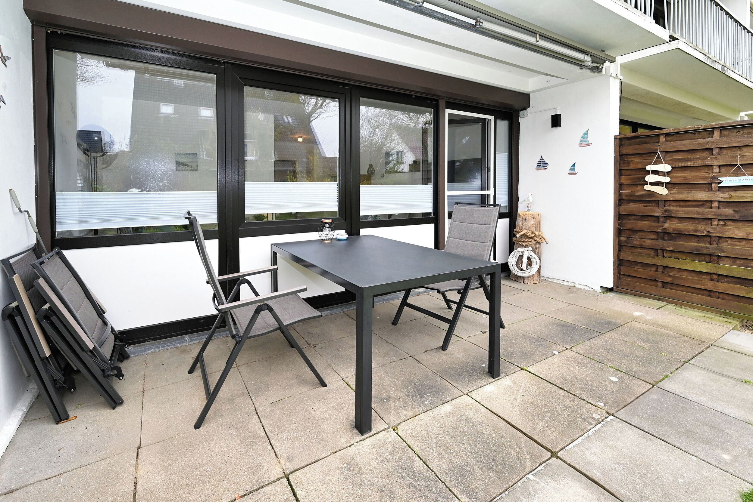 A patio area with a table and chairs, large windows, and a wooden fence.