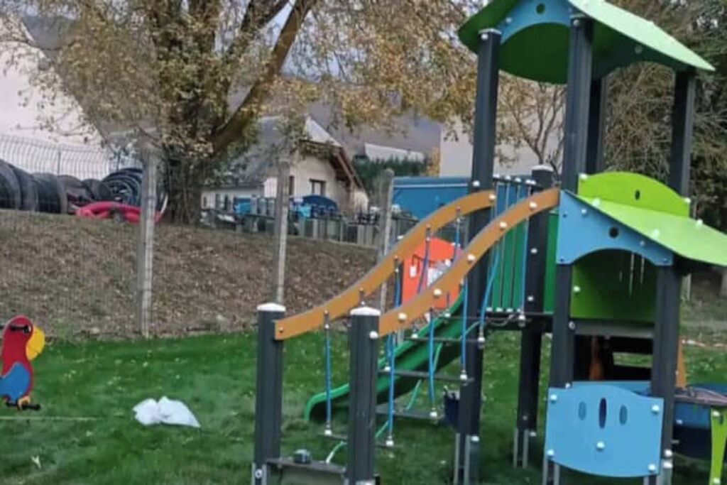 Ein Spielplatz mit Rutsche, Klettergerüsten und einer farbenfrohen Vogel-Skulptur.