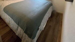 Une chambre à coucher comprenant un lit, une table de chevet, une commode, une fenêtre avec des rideaux et un luminaire fixé au mur.