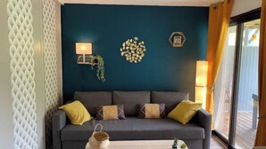 Un salon avec un mur bleu foncé, un canapé gris avec des coussins jaunes, une petite table avec un panier et deux lampes fixées au mur.