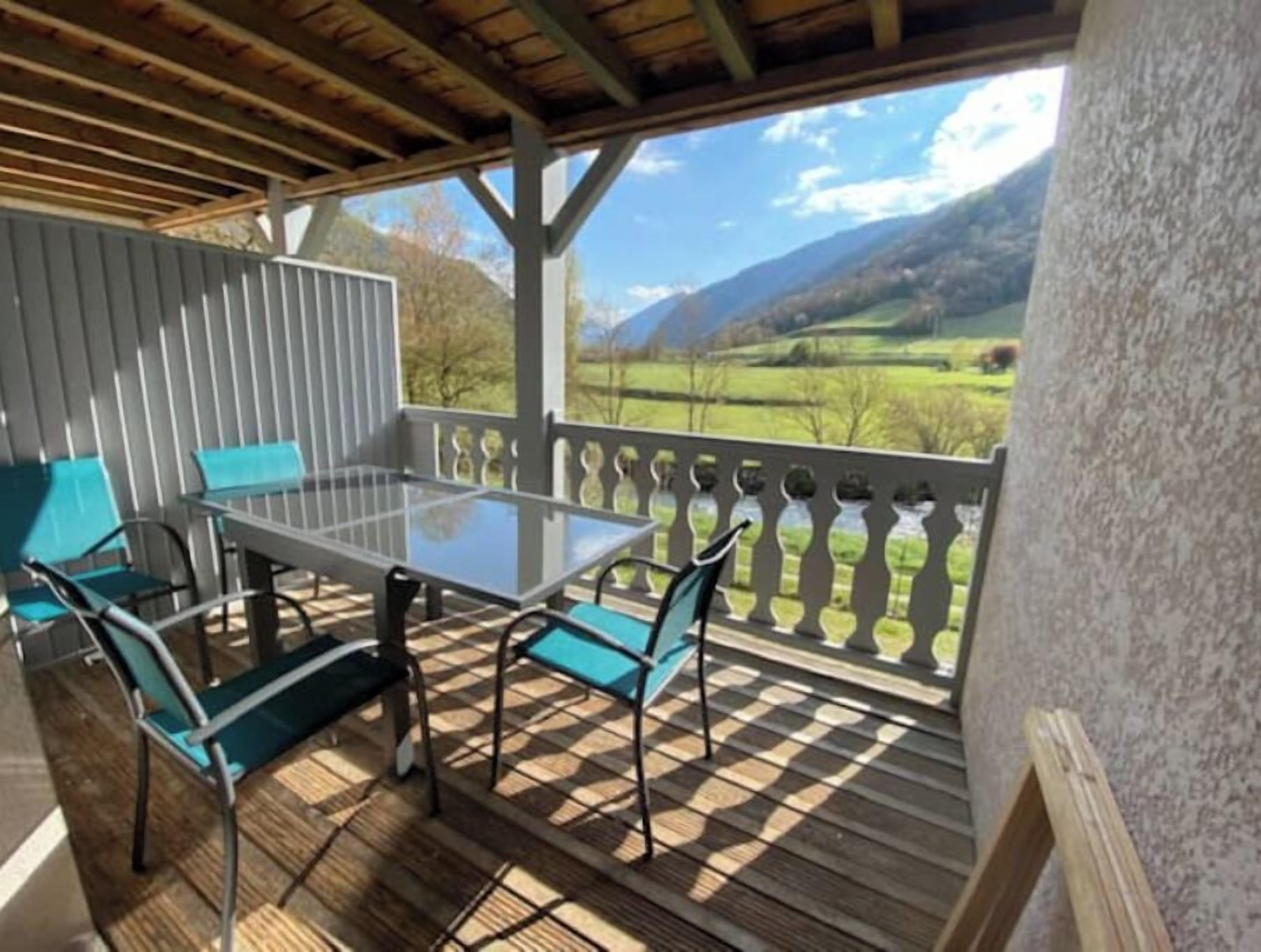 Een overdekt buitengebied met een tafel en stoelen, met uitzicht op een bergachtig landschap en een houten terras.