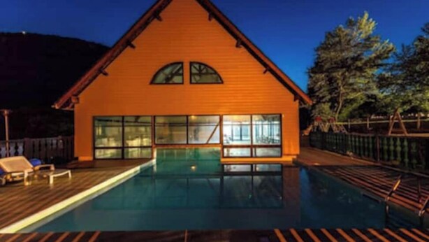 Une cabane en bois avec une piscine, de grandes fenêtres et une terrasse.