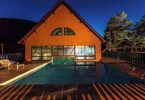 Une cabane en bois avec une piscine, de grandes fenêtres et une terrasse.