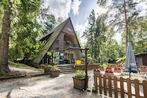 A rustic lodge with a triangular roof, outdoor seating, and a wooden fence. - Bungalow '10 - Finnhütte' with Private Terrace and Shared Garden (Niesky)
