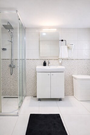 Ein modernes Badezimmer mit Duschkabine aus Glas, einem weißen Waschbecken mit Spiegel darüber und einem schwarzen Teppich auf dem Boden.