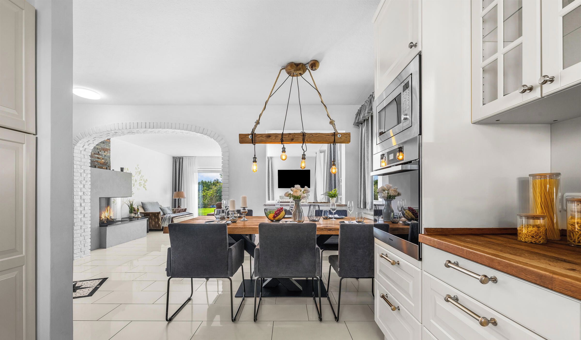 Cocina moderna con una isla central, muebles blancos y un comedor con vistas al exterior.