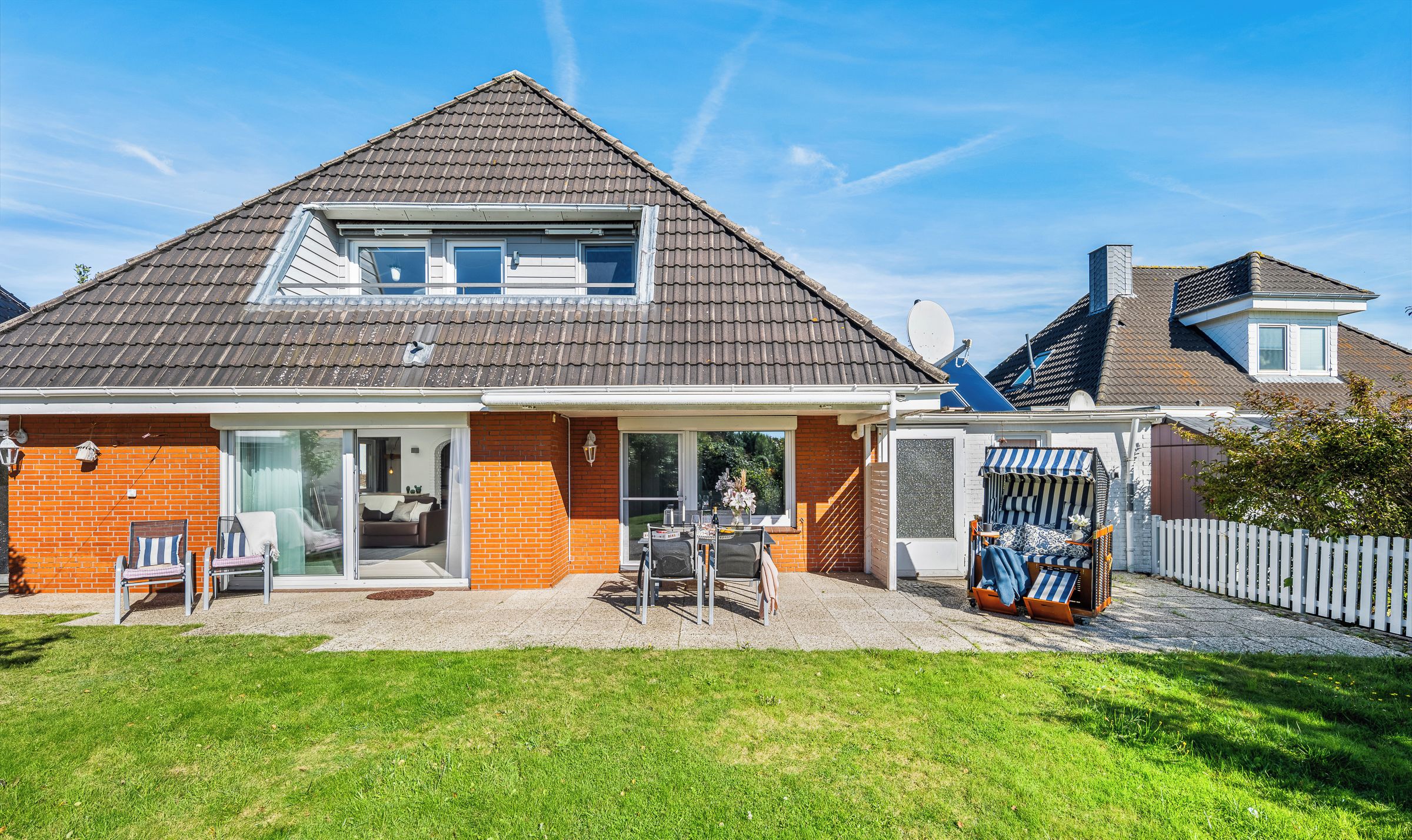 Une maison à deux étages, dotée d’un toit en pente, d’une façade en briques et d’un patio couvert aménagé avec du mobilier d’extérieur.