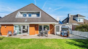 Une maison à deux étages, dotée d’un toit en pente, d’une façade en briques et d’un patio couvert aménagé avec du mobilier d’extérieur.