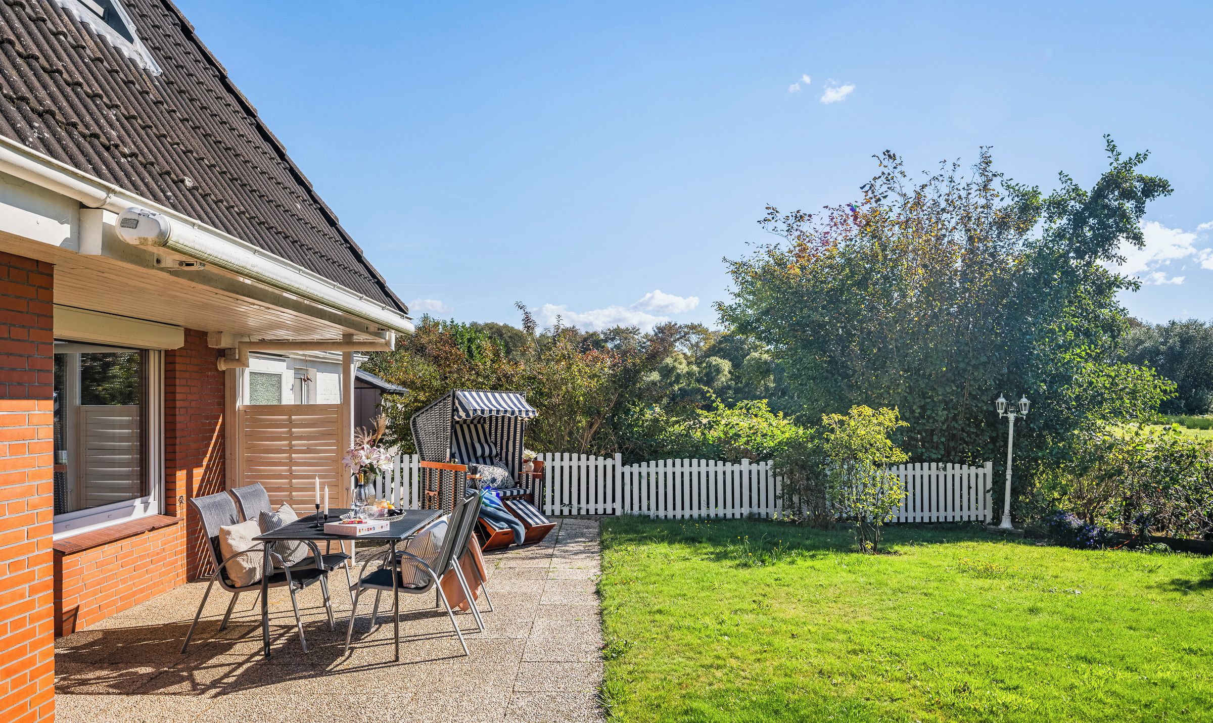 Une terrasse avec des meubles d’extérieur, une clôture blanche en bois et une pelouse bien entretenue.