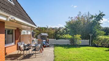 Une terrasse avec des meubles d’extérieur, une clôture blanche en bois et une pelouse bien entretenue.