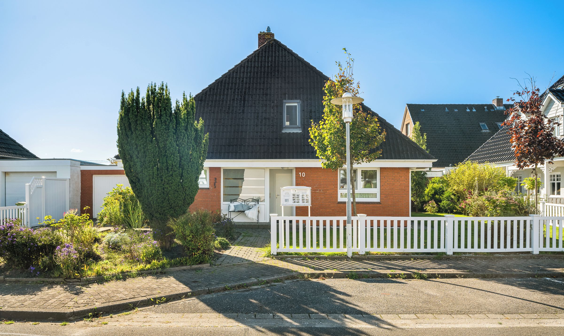 A residential house with a dark roof, a white picket fence, and a well-maintained garden.
