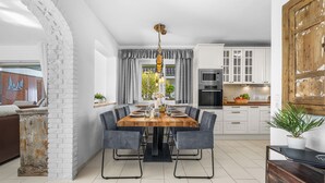 Una cocina moderna con armarios blancos, una mesa de comedor con sillas y un amplio ventanal con cortinas.