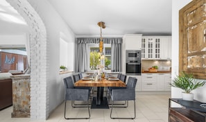 Une cuisine moderne avec des meubles blancs, une table à manger avec des chaises et une grande fenêtre agrémentée de rideaux.