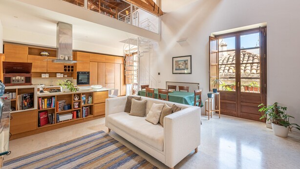 A spacious living area with a high ceiling, a kitchen with wooden cabinets, a white sofa, and a dining area with a table and chairs.