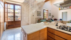A modern kitchen with a central island, wooden cabinets, and a spiral staircase leading to an upper level.