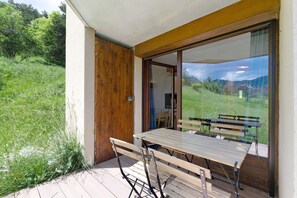 Eine Terrasse mit Tisch und Stühlen, eine Holztür und Blick auf eine grüne Landschaft.