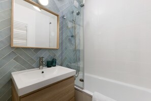 Ein Badezimmer mit Waschbecken, Spiegel, Dusche und gefliesten Wänden.