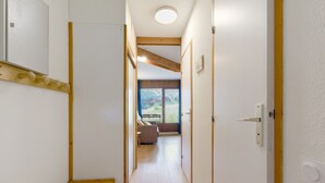 A narrow hallway with a wooden bench, a wooden beam ceiling, and a door leading to a room with a sofa and a table.