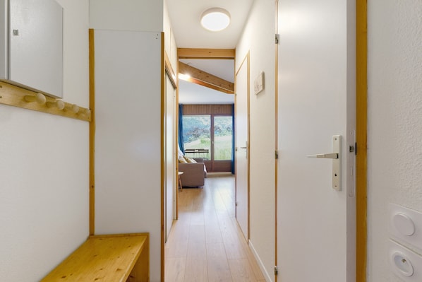A narrow hallway with a wooden bench, a wooden beam ceiling, and a door leading to a room with a sofa and a table.