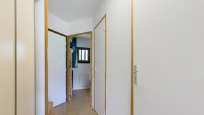 Un corridoio stretto con pavimento in legno, pareti bianche e una porta che dà su una stanza con una finestra.