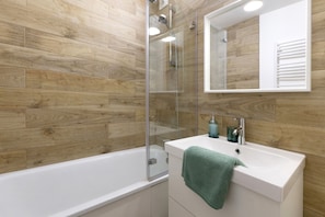 A modern bathroom with a wooden wall, a glass shower enclosure, a white sink with a green towel, and a mirror above the sink.