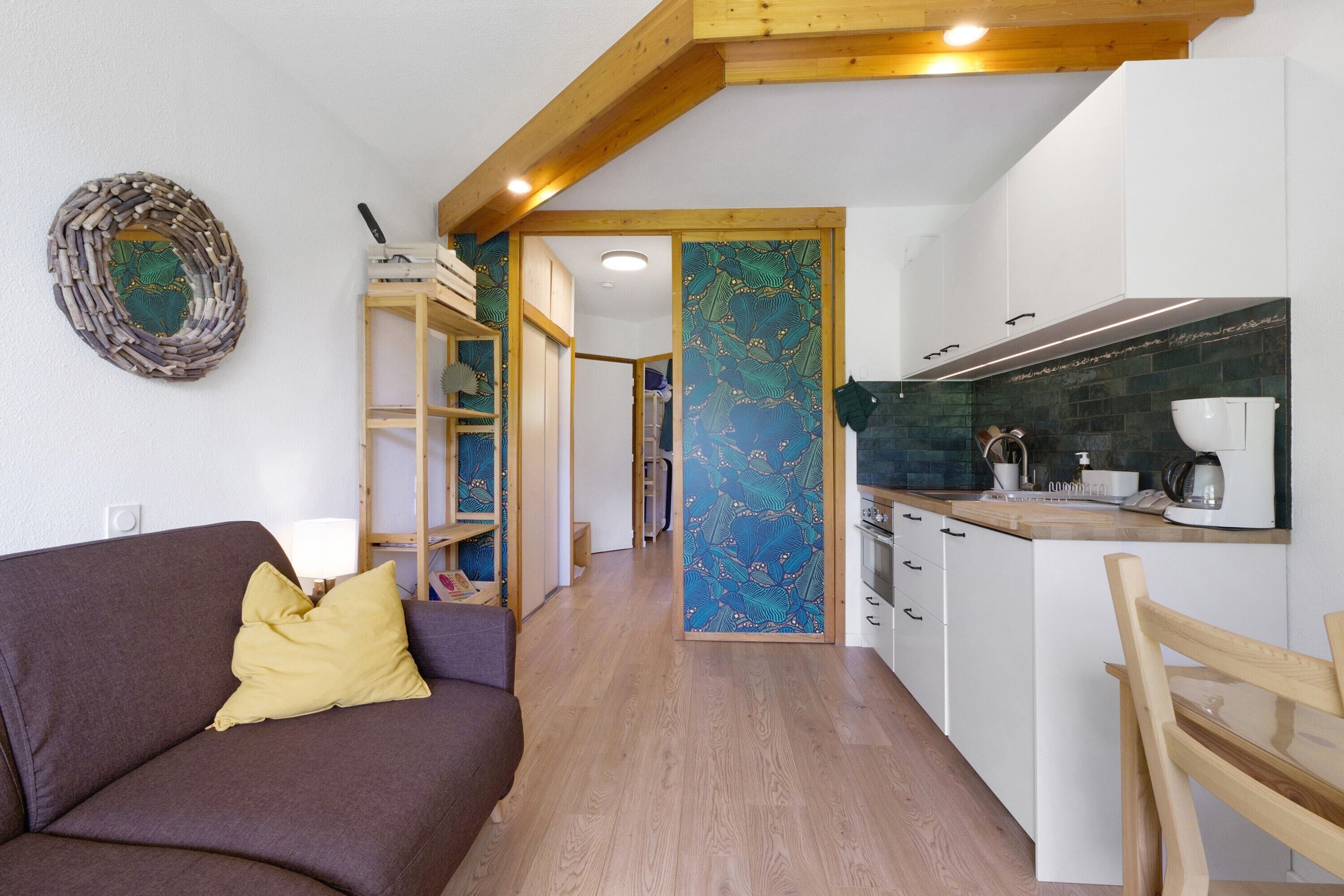 Ein gemütlicher Wohnraum mit Küchenzeile, einem Sofa und einem gelben Kissen sowie einem Holzbalken an der Decke.