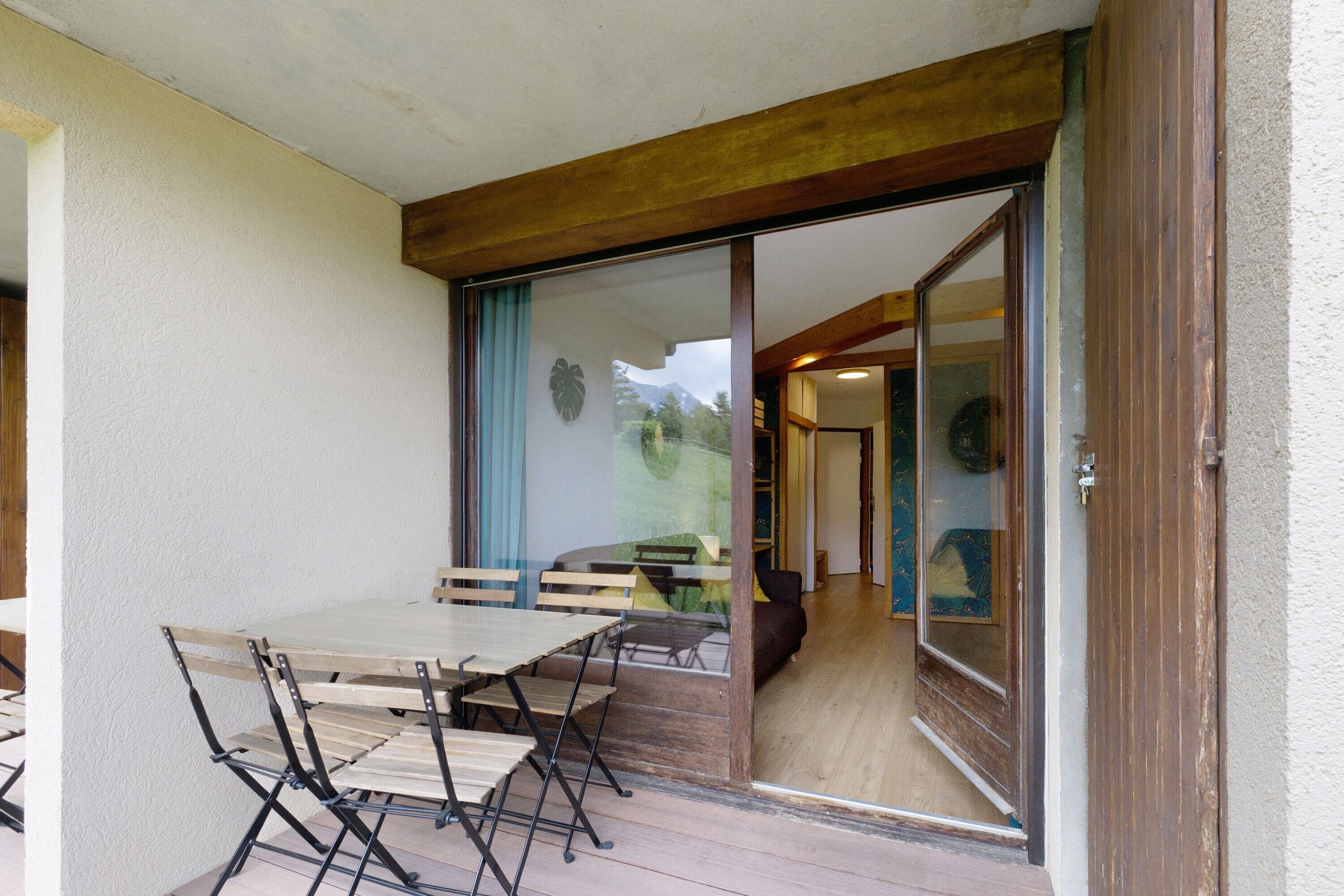 Un coin repas avec une table et des chaises, une porte-fenêtre coulissante donnant sur une pièce, et une poutre en bois au plafond.