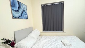 A bedroom with a bed, a window with curtains, a wall-mounted painting, and a small table with a vase of flowers. - Superb 2-bedroom apartment in Preston (Preston)
