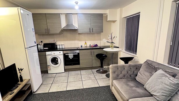 A compact living space with a kitchenette, a washing machine, a sofa, and a TV. - Superb 2-bedroom apartment in Preston (Preston)