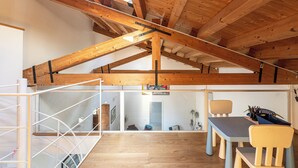 A spacious room with a high ceiling and exposed wooden beams. There is a desk with chairs and a window overlooking the interior. - San Salvatore Apartment by Wonderful Italy (Palermo)