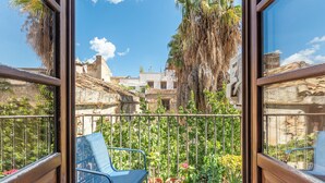 A balcony with a blue chair, potted plants, and a view of buildings and trees. - San Salvatore Apartment by Wonderful Italy (Palermo)