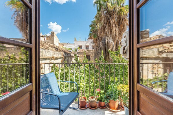 Un balcon avec une chaise bleue, des plantes en pot et une vue sur des immeubles et des arbres.