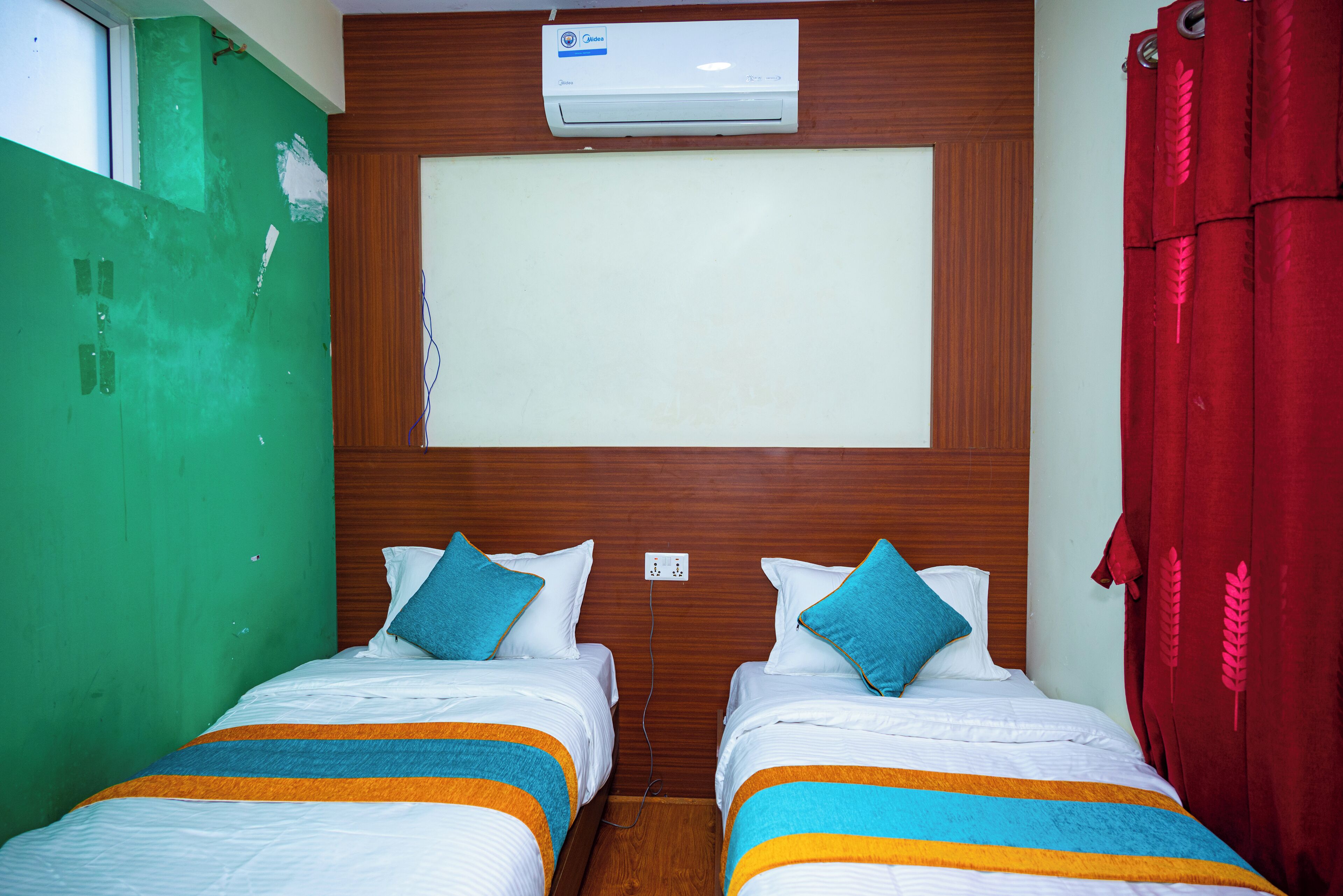 A hotel room with two beds, a wooden headboard, a large air conditioning unit, and a red curtain.