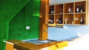 A bar area with a green artificial grass wall, wooden shelves with bottles and glasses, and a wooden counter. - Hotel Sara Inn (Kathmandu)