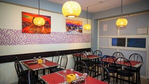 A restaurant with red tables and black chairs, decorative wall art, and patterned wallpaper. - Hotel Sara Inn (Kathmandu)