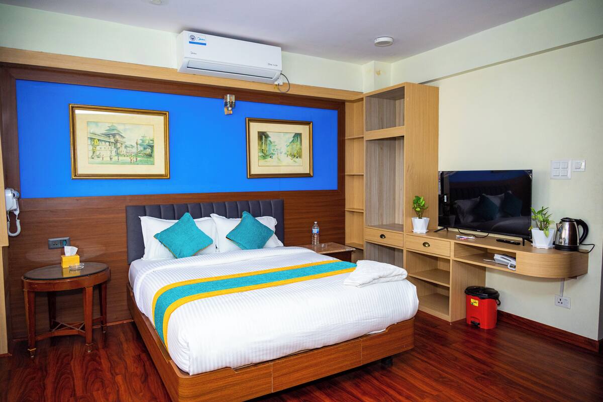 A hotel room with a large bed, a TV, a desk, and two framed pictures on the wall.